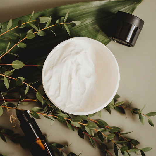 Open jar of cream beside eucalyptus leaves